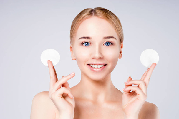 Woman beautiful face portrait with clean fresh skin and two cotton swabs. Facial treatment. Beautiful spa model girl looking at camera while standing against grey background. - 写真・画像