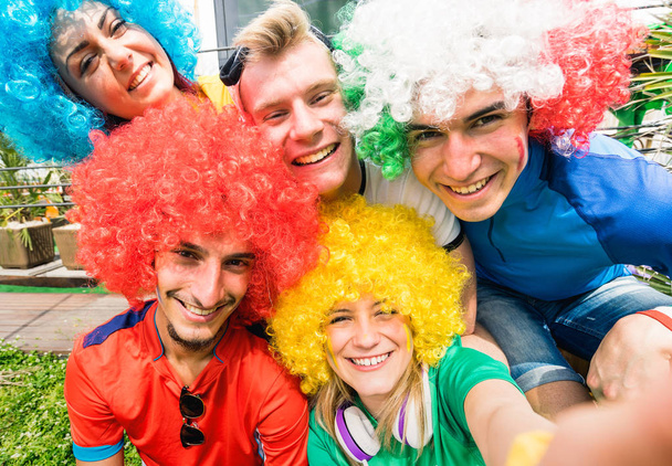 Voetbal supporter fans vrienden nemen selfie na beker overeen met opknoping rond samen - groep met veelkleurige t-shirts en pruiken hebben opgewonden plezier op sport Wereldkampioenschap jongeren - Foto, afbeelding