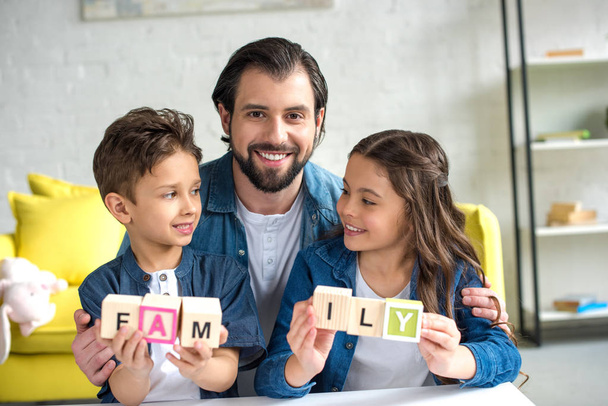 счастливый отец с двумя очаровательными детьми, держащими кубики со словом семья
 - Фото, изображение