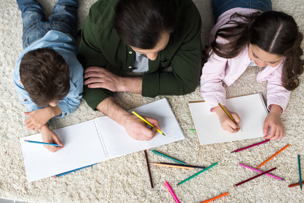 yleiskuva isästä, jolla on lapsia piirtämässä värillisiä kyniä kotona
 - Valokuva, kuva