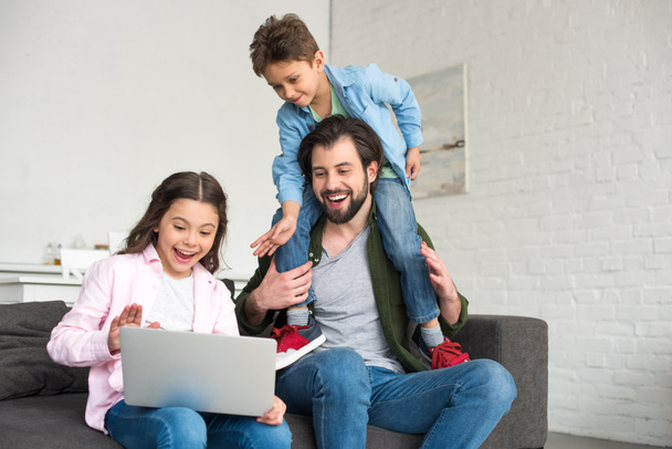 glücklicher Vater mit zwei süßen Kindern, die zusammen auf dem Sofa sitzen und Laptop benutzen  - Foto, Bild