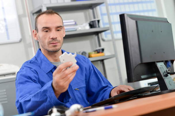 Man sat in front of computer, holding electrical component - Fotó, kép