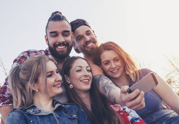 happy group of best friends millennials take a selfie photo outdoor in summer mood. sunlight from right side flaring. - Foto, afbeelding