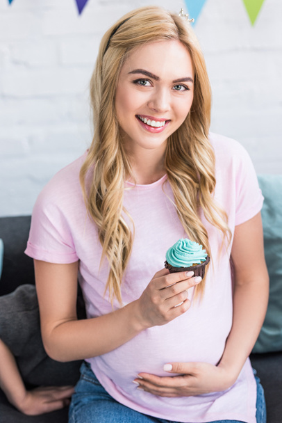 beautiful pregnant woman holding cupcake and looking at camera at baby shower party - Zdjęcie, obraz