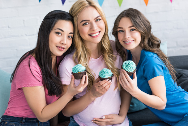 retrato de amigos multiculturales y mujer embarazada con cupcakes en fiesta de baby shower
 - Foto, Imagen