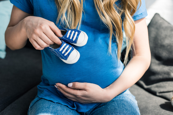 обрізане зображення вагітної жінки, що торкається живота з дитячим взуттям
 - Фото, зображення