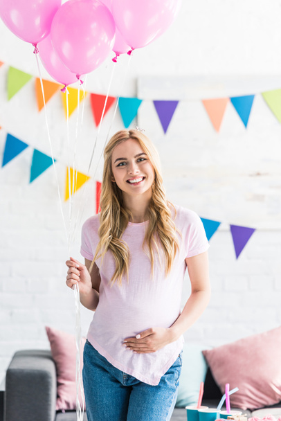 beautiful pregnant woman standing with bundle of balloons and looking at camera at baby-party - Photo, Image