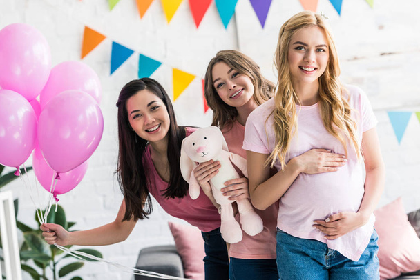 Lächelnde multikulturelle Freunde und schwangere Frau posieren auf Baby-Party mit Hasenspielzeug - Foto, Bild