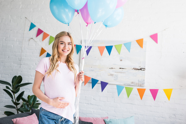beautiful pregnant woman touching belly and holding bundle of balloons at baby-party - Фото, зображення