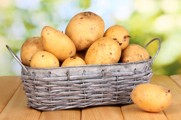 Ripe potatoes on basket on wooden table on natural background - Foto, afbeelding