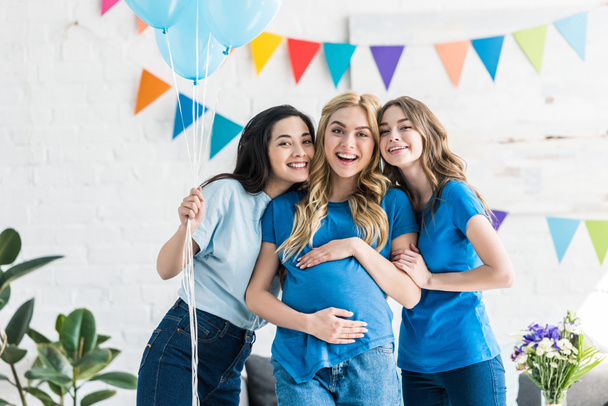 улыбающиеся мультикультурные друзья с воздушными шарами и беременная женщина, смотрящая в камеру на детской вечеринке
 - Фото, изображение