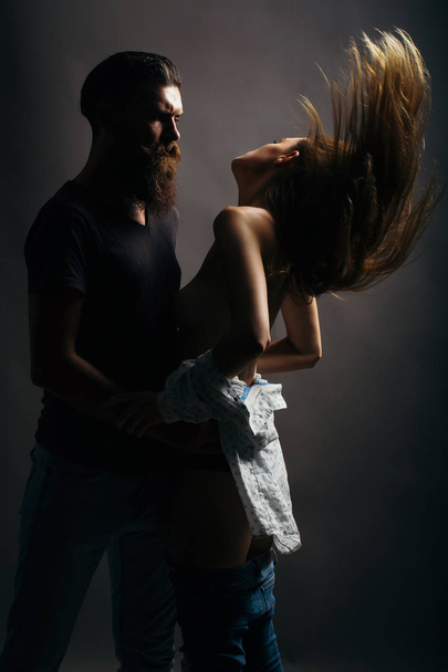 young couple silhouette of handsome bearded man with long beard and pretty sexy woman or girl topless with naked back and red hair in studio on black background - Zdjęcie, obraz