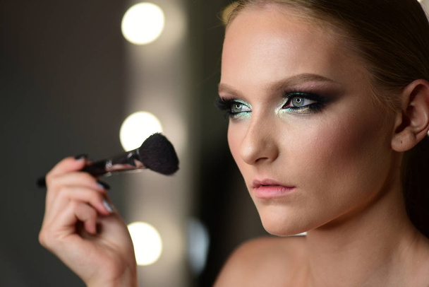 Young beautiful woman applying makeup on face by brush. - Valokuva, kuva