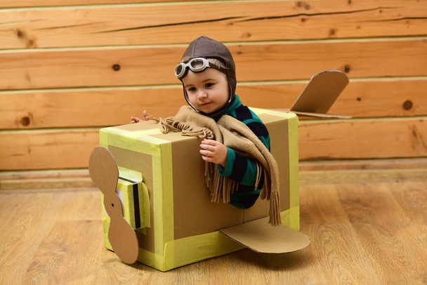 Мальчик, играющий в пилота, летающего на картонной коробке в детской комнате
 - Фото, изображение