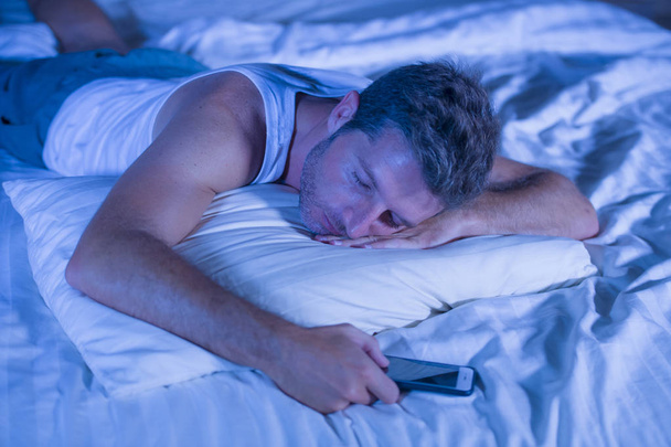 attractive tired man in bed falling asleep while using mobile phone still holding the cellular in his hand while sleeping in internet and social media addiction - Фото, зображення