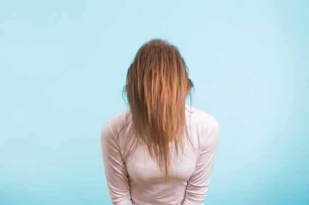El cabello dividido frágil y el concepto de problema de cabello - Mujer joven con el pelo largo poco saludable aislado en azul
 - Foto, Imagen