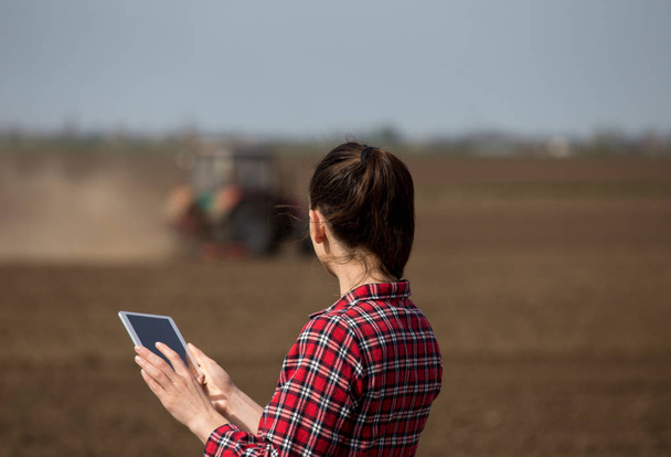 Femme agricultrice avec tablette et tracteur sur le terrain
 - Photo, image