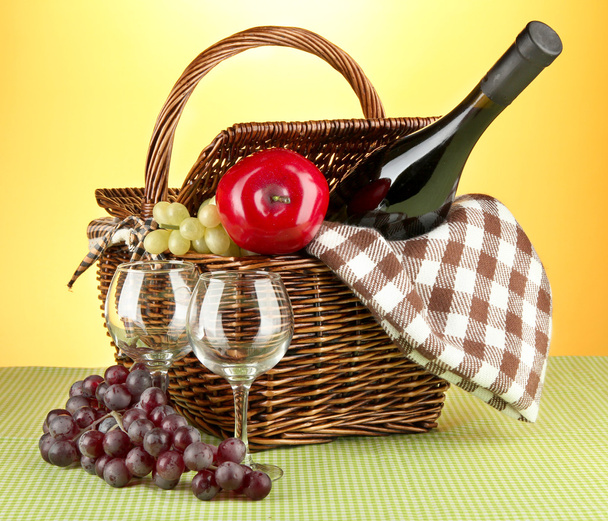 Picnic basket and bottle of wine on cloth on yellow background - Foto, afbeelding