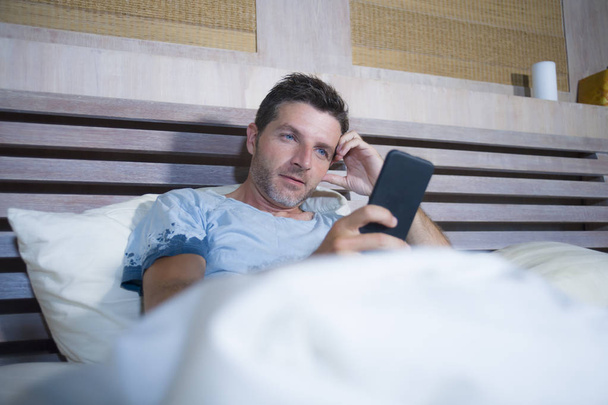 young attractive and happy man lying on bed using internet mobile phone smiling sending text in social media and cellular communication addiction  - 写真・画像