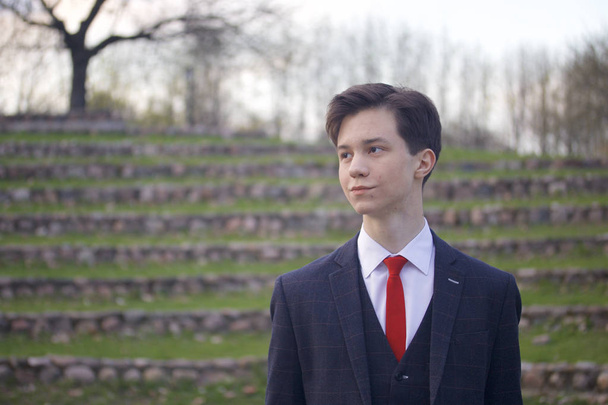 A young man, a teenager, in a classic suit. It stands on the stone steps of the summer amphitheater, putting his hands in his pockets. - Фото, зображення