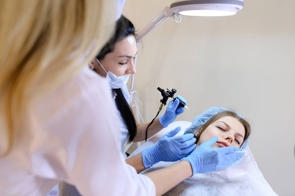 Młody kosmetolog Dokonywanie oznaczanie procedury dla kobiety przez maszyny. - Zdjęcie, obraz