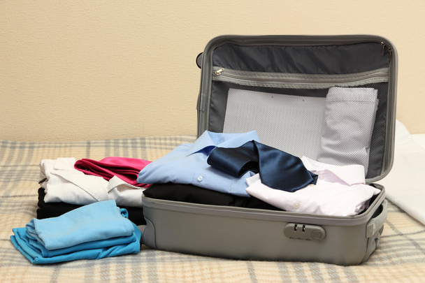 Open grey suitcase with clothing on bed - Photo, image