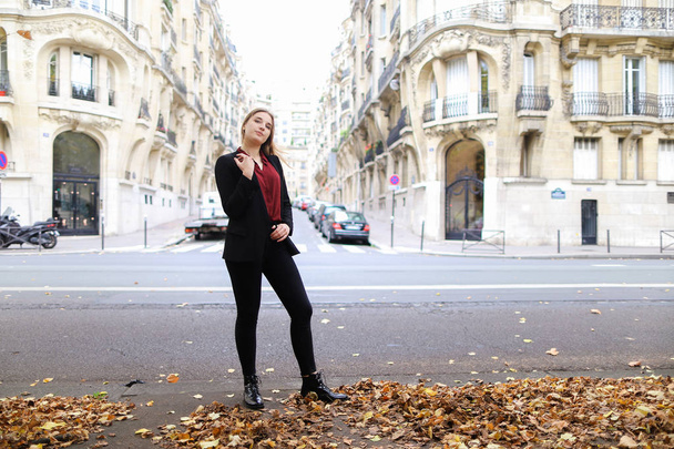 Женщина фотомодель стоит на улице с опавшими листьями и здания на заднем плане
. - Фото, изображение