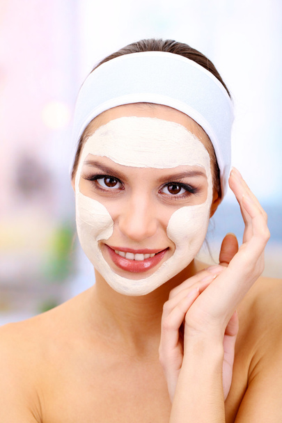 Young woman with clay facial mask, on bright background - Photo, image