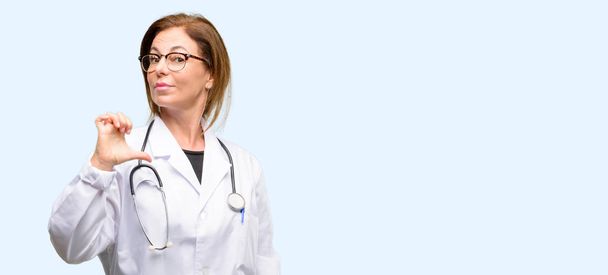 Doktor kadın, tıbbi profesyonel gurur, heyecanlı ve küstah, zafer yüzü ile işaret eden mavi arka plan izole - Fotoğraf, Görsel