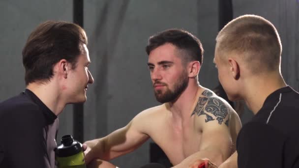 Τρεις άνδρες φίλοι αναπαύεται στο γυμναστήριο μετά από γέλια και ομιλίες - Πλάνα, βίντεο