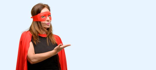 Keski-ikä supersankari nainen yllään punainen naamio ja viitta tilalla jotain tyhjään käteen eristetty sininen tausta
 - Valokuva, kuva