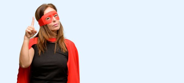 Супергероиня средних лет женщина в красной маске и плаще счастливый и удивленный приветствуя выражение вау жест указывая на изолированный синий фон
 - Фото, изображение