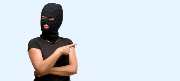 Террористка-грабительница в балаклавской лыжной маске, указывающая на сторону пальца на синем фоне
 - Фото, изображение