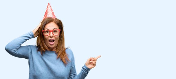 Middle age woman celebrates birthday pointing away side with finger isolated blue background - Photo, Image