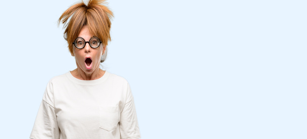 Сумасшедшая женщина средних лет в глупых очках, напуганная от шока, выражающая панику и страх изолированного синего фона
 - Фото, изображение