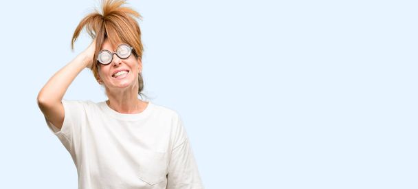 Crazy middle age woman wearing silly glasses terrified and nervous expressing anxiety and panic gesture, overwhelmed isolated blue background - 写真・画像