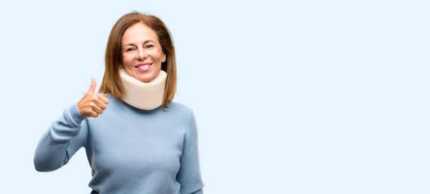 Mujer lesionada con cuello ortopédico cuello sonriendo ampliamente mostrando los pulgares hacia arriba gesto a la cámara, expresión de como y aprobación aislado fondo azul
 - Foto, imagen