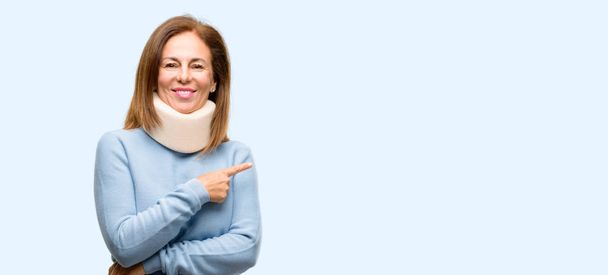 Injured woman wearing neck brace collar pointing away side with finger isolated blue background - Photo, Image