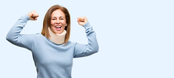 Τραυματισμένη γυναίκα που φοράει λαιμό στήριγμα κολάρο χαρούμενος και συγκινημένος γιορτάζουμε νίκη εκφράζοντας την μεγάλη επιτυχία, δύναμη, ενέργεια και θετικά συναισθήματα. Γιορτάζει τα νέα εργασία χαρούμενη απομονωμένες μπλε φόντο - Φωτογραφία, εικόνα