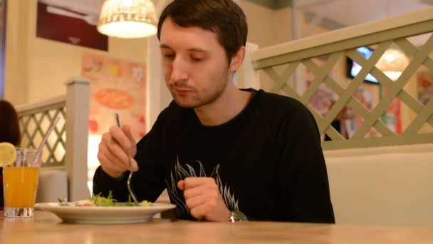 Een man zit in een restaurant en eet salade - Video