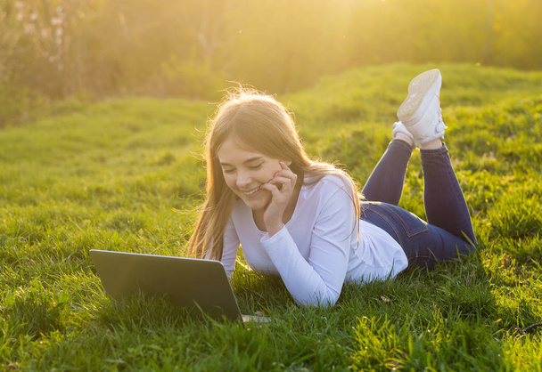 Jonge mooie lachende vrouw met laptop ligt op het gras in - Foto, afbeelding