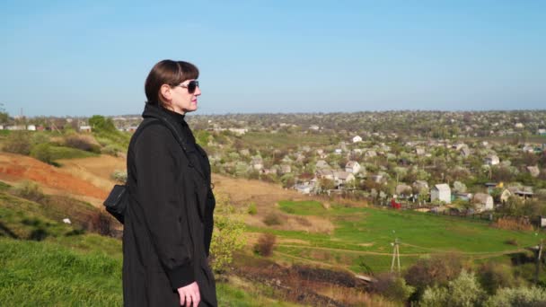 Koncepcja: powrót do domu. Młoda kobieta stoi na wzgórzu i wygląda na domów, u podnóża wzgórza - Materiał filmowy, wideo