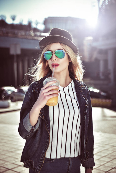 かわいい女の子は、帽子とサングラスで街にジュースを保持します。 - 写真・画像