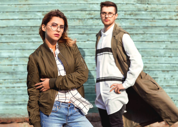 fashion couple in glasses with glasses in green clothes posing on blue wooden wall - Photo, image