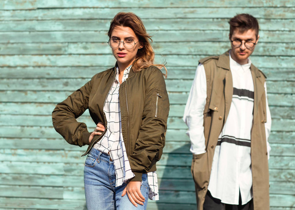 fashion couple in glasses with glasses in green clothes posing on blue wooden wall - Foto, afbeelding
