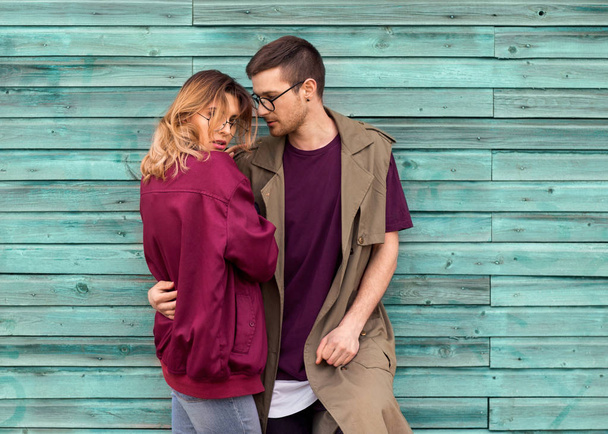 fashion couple in their glasses with burgundy clothes posing on  a blue wooden wall - Photo, image