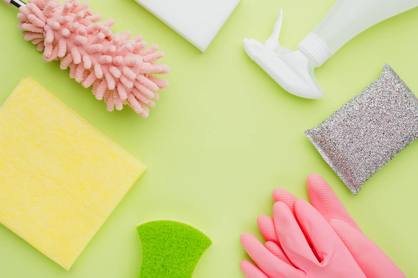 The concept of modern minimalistic cleaning and cleanliness, flat lay on a green background lime color lie pink rubber gloves and sprayer, sponge and duster and rags, place for text - Фото, изображение