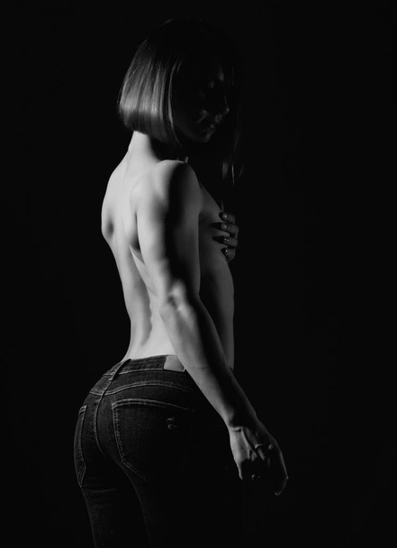Young female model with muscular body poses on a dark background. black and white - Foto, Imagem