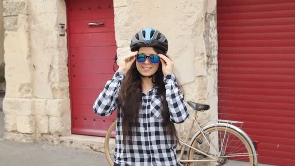 Nuori nainen pyöräilijä silmälasit päässä ja kypärä hymyillen ja katsoen kameraa
 - Materiaali, video
