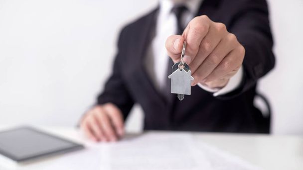 Male broker holding out key chain house, signing contract, buying a property - Foto, Bild